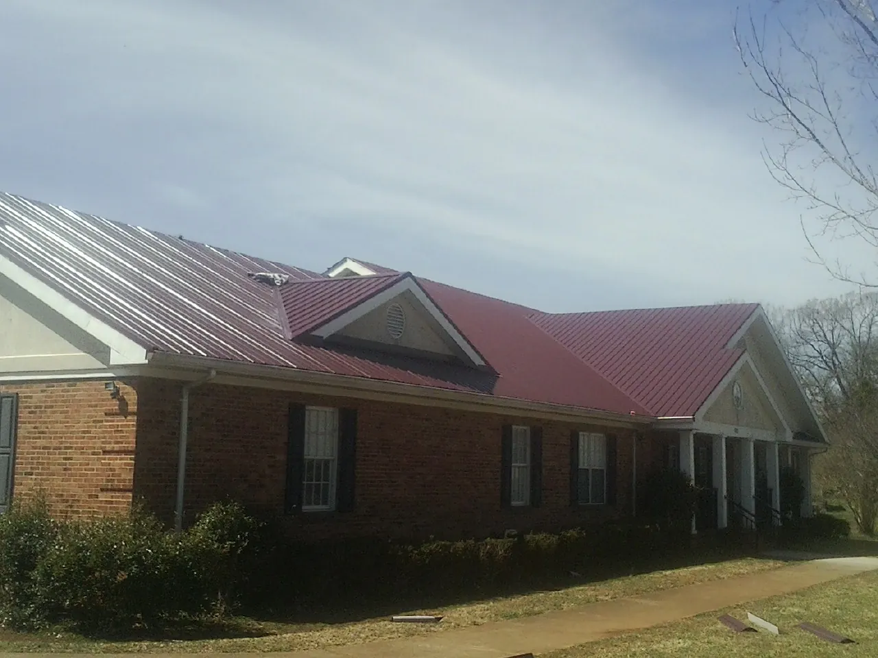 Red metal roof with gabled entries on a long brick building, from a Hail Damage Roof Repair job in Palmdale