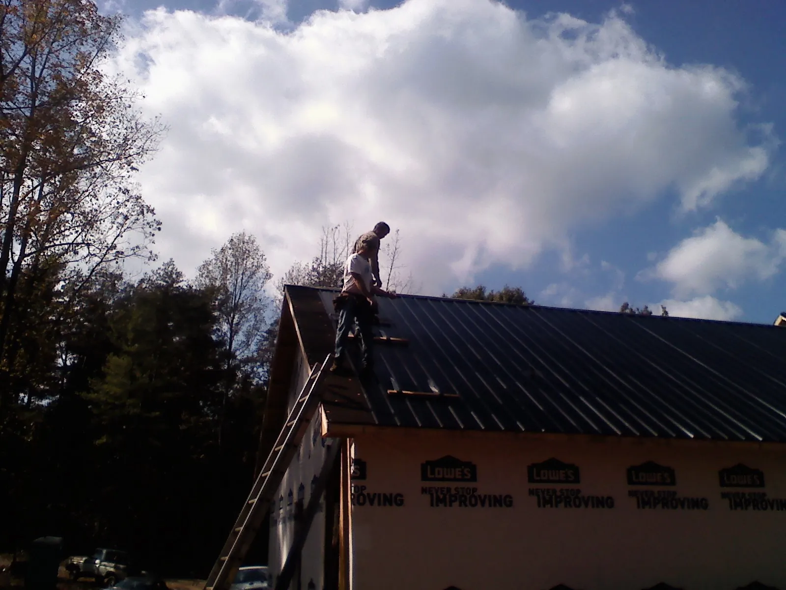 Roofer fastening dark metal panels high against a cloudy sky, from a Roof Inspection job in Palmdale
